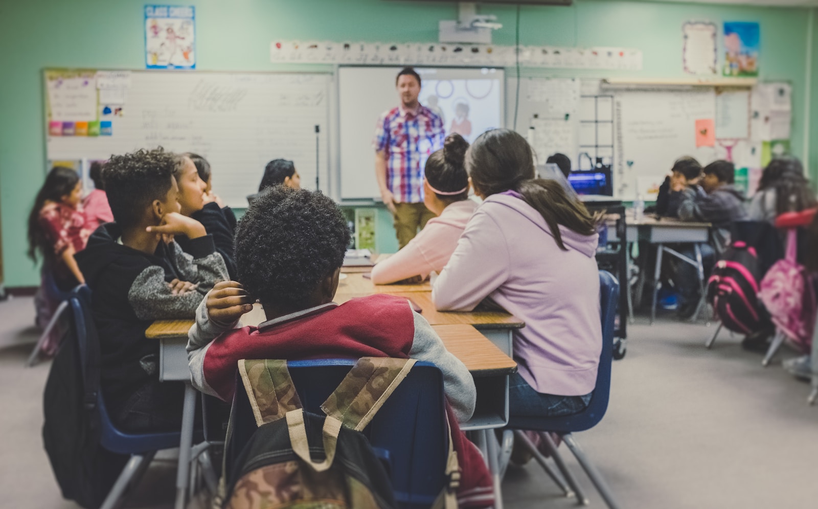 Upper elementary school students facing a teacher at the front of the room