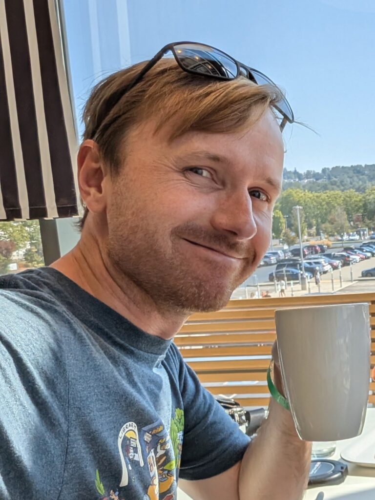 Mark smiling with a cup of coffee inside a sunny room