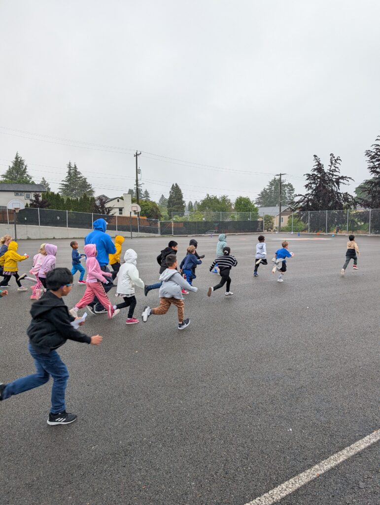 Lots of young children running across the Roxhill playground blacktop