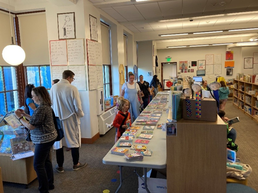 Adults and kids in jammies looking at long tables of books in the library